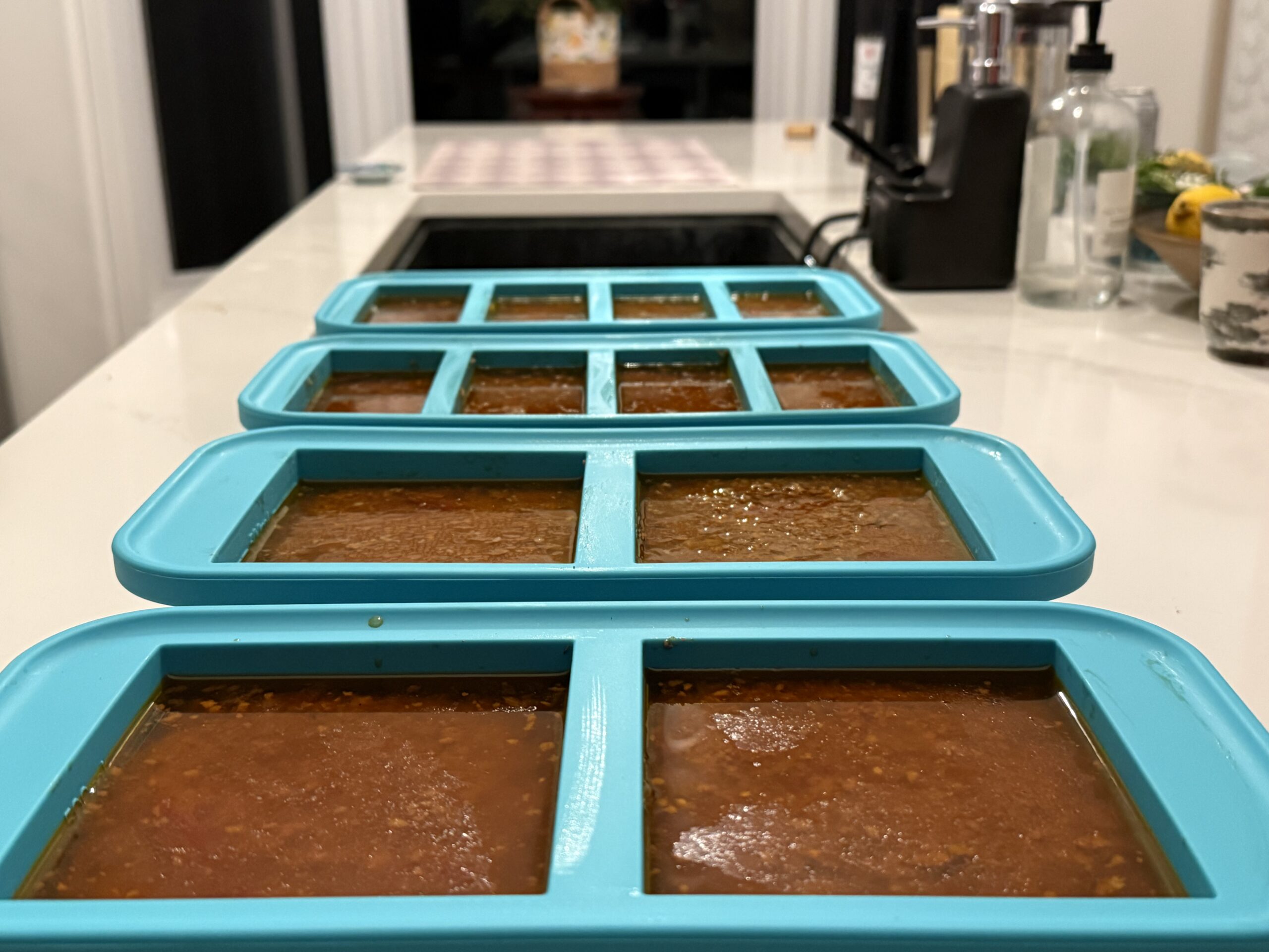 Four teal silicone Souper Cubes freezer trays filled with rich Bolognese sauce lined up on a white kitchen counter